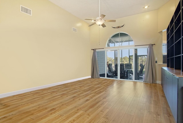 unfurnished living room with light wood-type flooring, high vaulted ceiling, baseboards, and visible vents