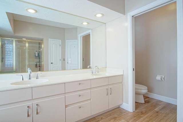 bathroom with double vanity, a stall shower, toilet, wood finished floors, and a sink