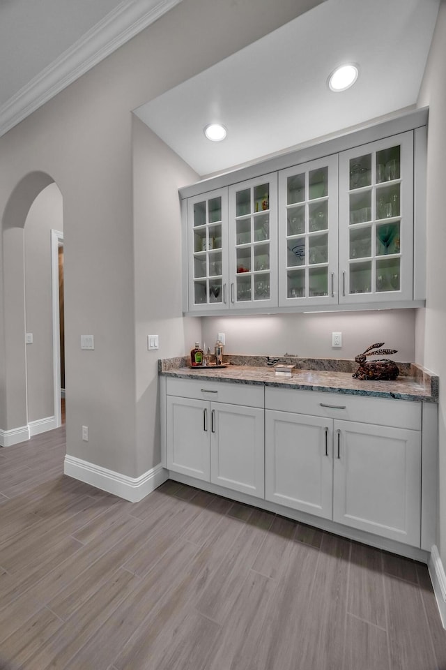 bar featuring arched walkways, recessed lighting, baseboards, light wood-style floors, and a dry bar