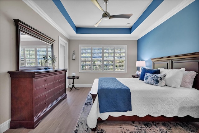 bedroom featuring crown molding, a raised ceiling, ceiling fan, wood finished floors, and baseboards