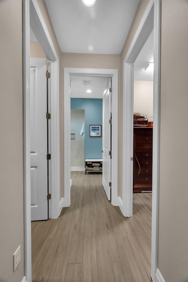 hallway featuring light wood finished floors, visible vents, and baseboards