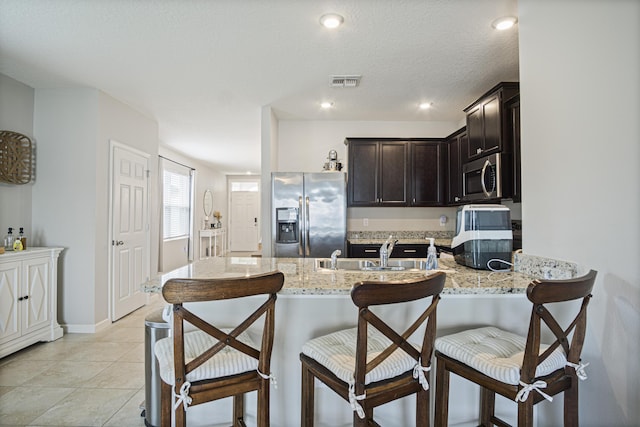 kitchen featuring light stone counters, visible vents, appliances with stainless steel finishes, a sink, and a peninsula