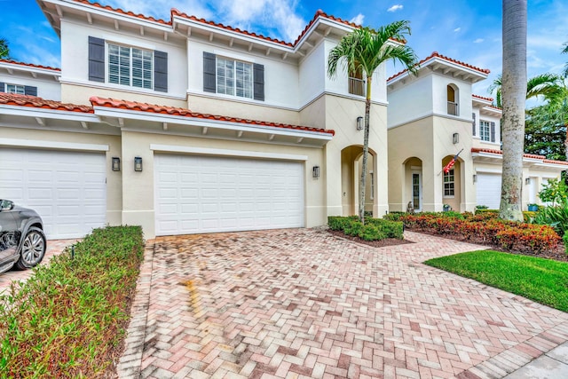 mediterranean / spanish house with a tiled roof, decorative driveway, an attached garage, and stucco siding