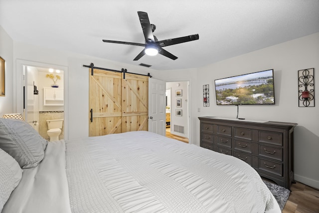 bedroom featuring a barn door, wood finished floors, visible vents, a ceiling fan, and ensuite bath