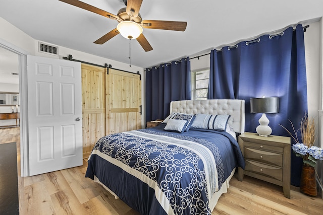 bedroom with ceiling fan, a barn door, light wood-type flooring, and visible vents