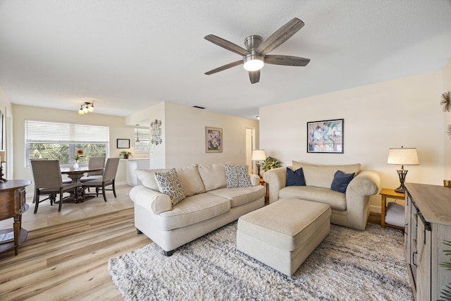 living room with a textured ceiling, light wood-style flooring, visible vents, baseboards, and a ceiling fan