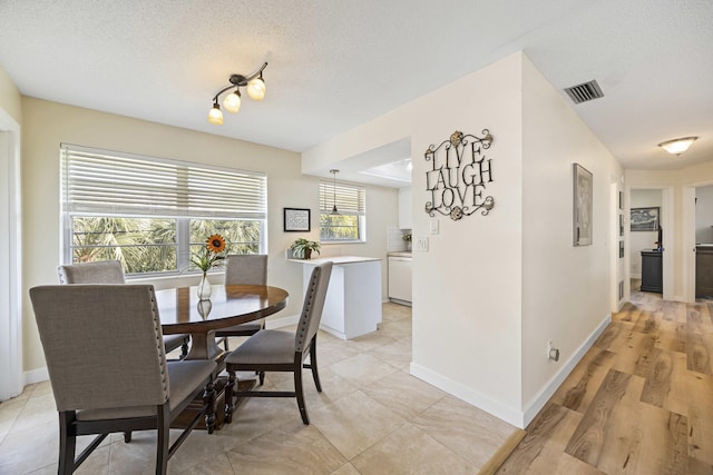 dining space featuring light wood-style floors, baseboards, visible vents, and a textured ceiling