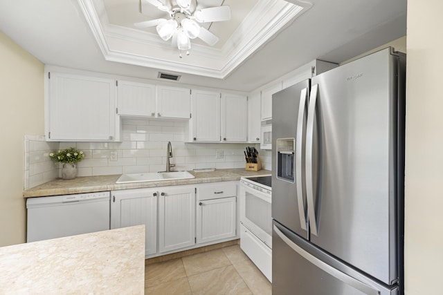 kitchen with white appliances, visible vents, ornamental molding, a tray ceiling, and a sink