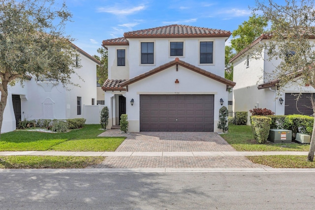 mediterranean / spanish home with decorative driveway, a tiled roof, a front lawn, and stucco siding