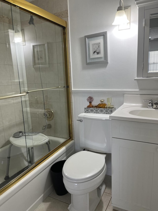 full bath with toilet, enclosed tub / shower combo, wainscoting, vanity, and tile patterned flooring