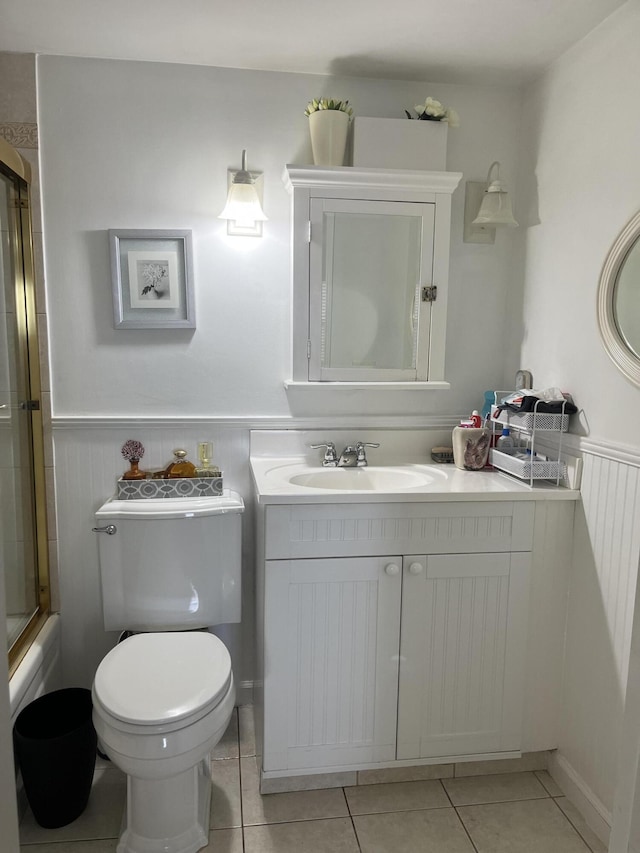 bathroom featuring toilet, a wainscoted wall, shower / bath combination with glass door, tile patterned flooring, and vanity