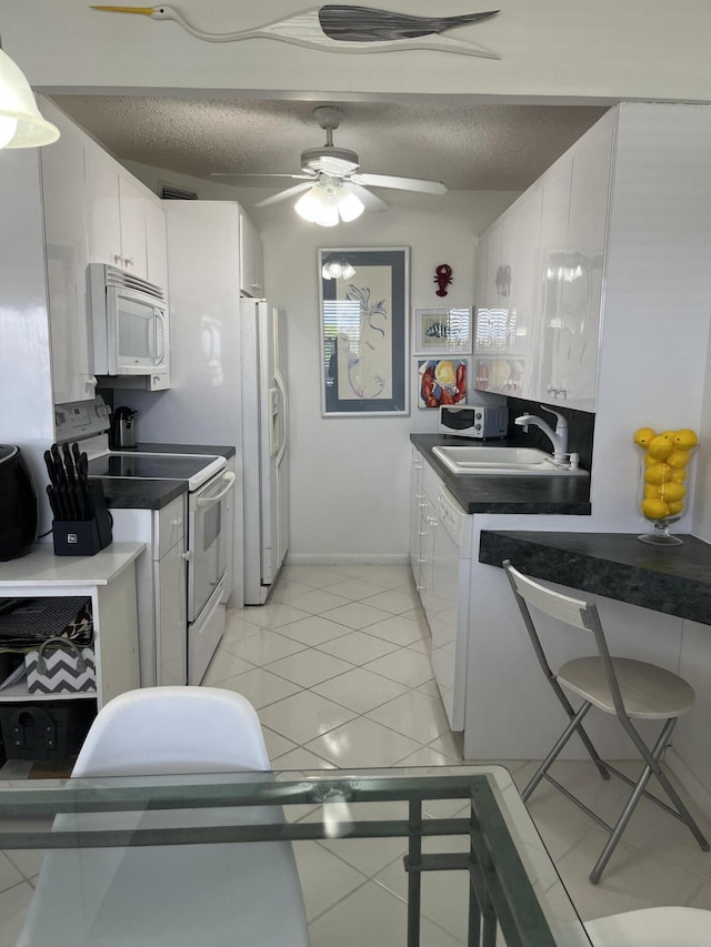 kitchen featuring dark countertops, white appliances, white cabinets, and a sink