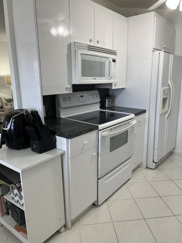 kitchen featuring dark countertops, white appliances, light tile patterned floors, and white cabinetry