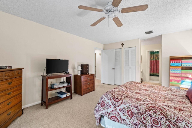 bedroom with light carpet, baseboards, visible vents, a textured ceiling, and two closets