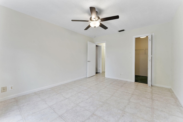 unfurnished bedroom featuring visible vents, a spacious closet, a ceiling fan, a textured ceiling, and baseboards