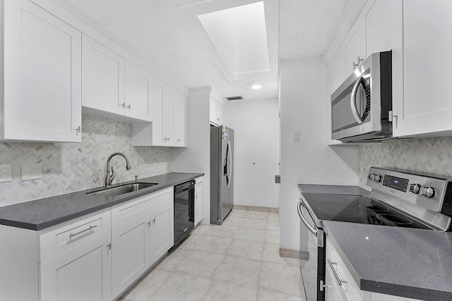 kitchen with light tile patterned floors, a sink, white cabinets, appliances with stainless steel finishes, and backsplash