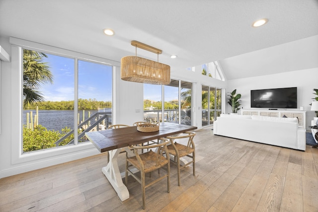 dining space featuring lofted ceiling, light wood-style floors, a water view, and recessed lighting