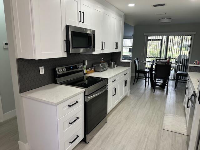 kitchen featuring light wood finished floors, visible vents, appliances with stainless steel finishes, and backsplash