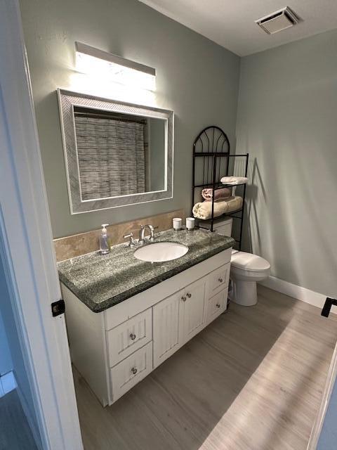 bathroom with toilet, wood finished floors, vanity, visible vents, and baseboards