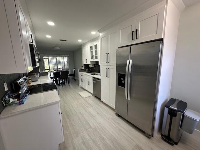 kitchen with recessed lighting, light wood-style flooring, appliances with stainless steel finishes, glass insert cabinets, and white cabinets