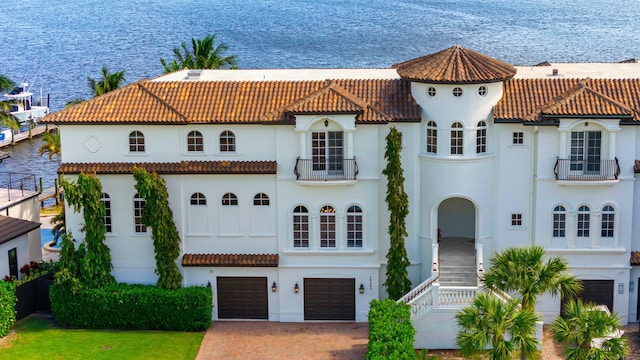 view of front facade with a balcony, a garage, a water view, decorative driveway, and stucco siding