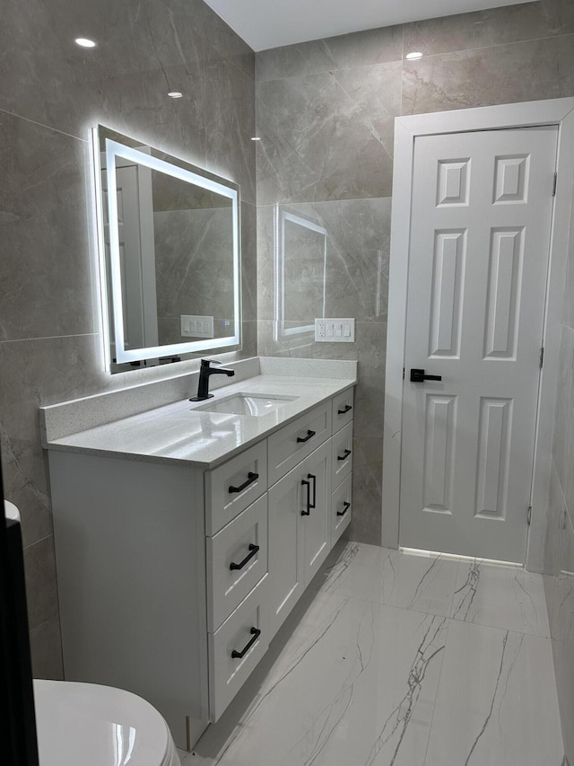 bathroom with toilet, marble finish floor, tile walls, and vanity