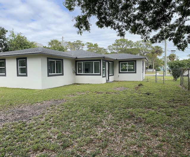 view of front of house with a front lawn, a shingled roof, fence, and stucco siding