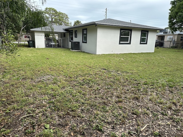 back of house featuring stucco siding, a shingled roof, cooling unit, and a yard