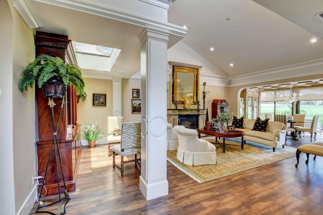 living area featuring decorative columns, a glass covered fireplace, lofted ceiling with skylight, wood finished floors, and crown molding