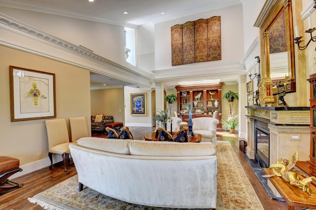 living room with ornamental molding, a high end fireplace, a high ceiling, and wood finished floors