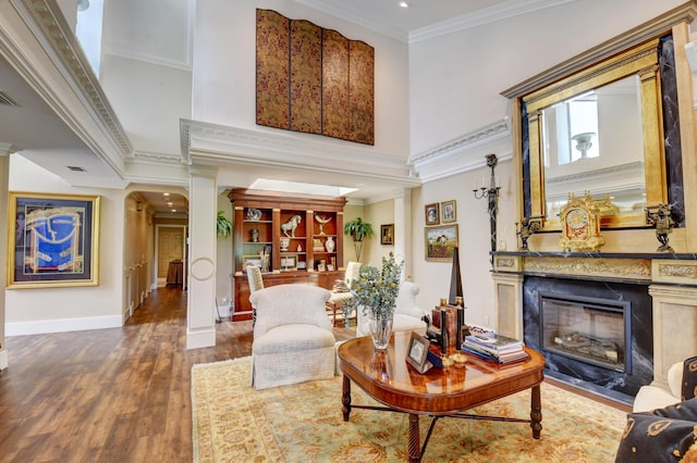 living area with decorative columns, a towering ceiling, a fireplace with flush hearth, wood finished floors, and crown molding