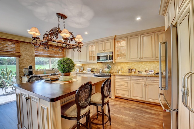 kitchen with stainless steel appliances, tasteful backsplash, cream cabinets, and light wood-type flooring