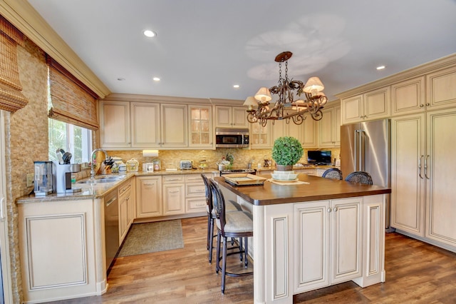 kitchen featuring stainless steel appliances, cream cabinets, a sink, and light wood-style flooring