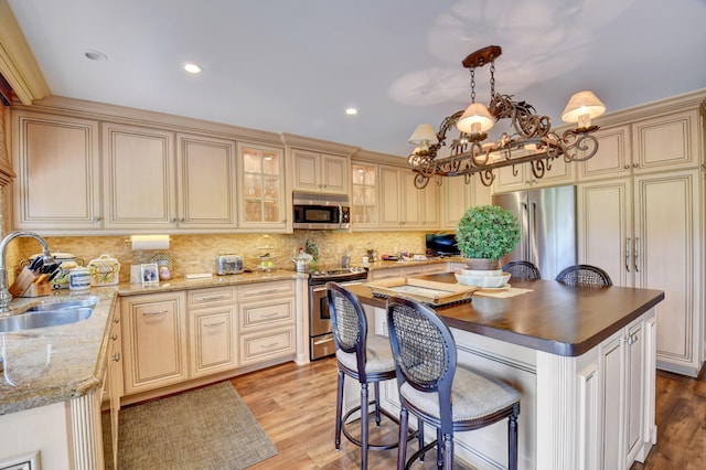 kitchen featuring a kitchen island, appliances with stainless steel finishes, cream cabinets, light wood-style floors, and a sink