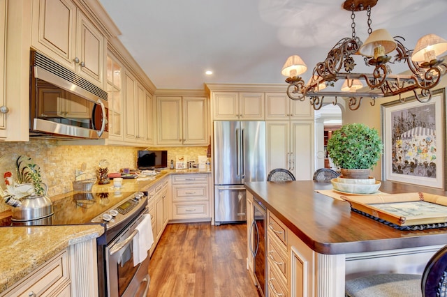 kitchen featuring decorative backsplash, wood counters, appliances with stainless steel finishes, wood finished floors, and cream cabinetry