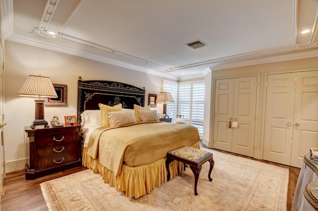 bedroom with two closets, visible vents, ornamental molding, and wood finished floors