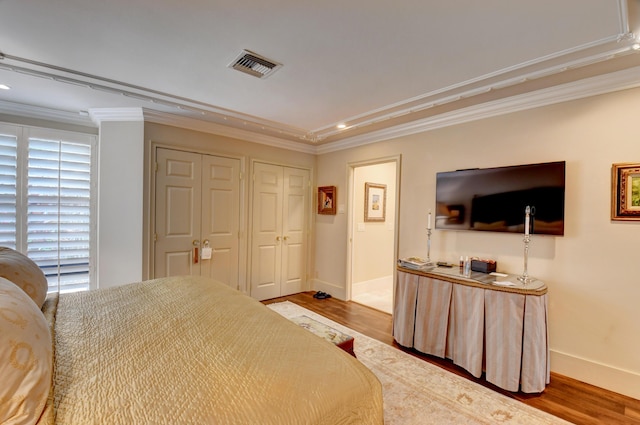 bedroom with baseboards, visible vents, crown molding, and wood finished floors