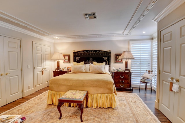 bedroom featuring two closets, visible vents, crown molding, and wood finished floors