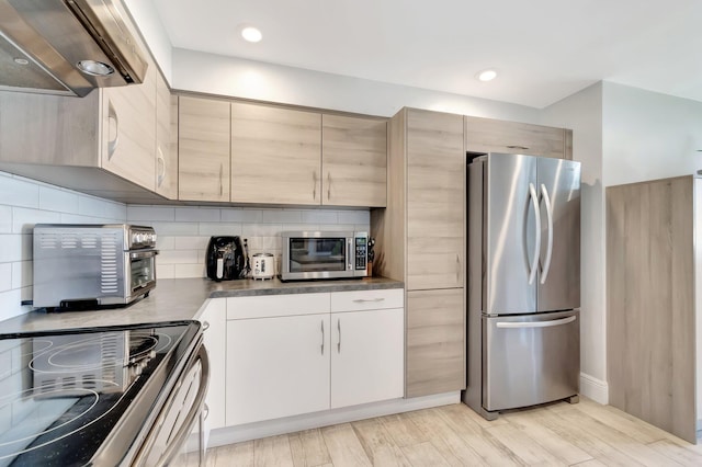 kitchen featuring light wood finished floors, tasteful backsplash, dark countertops, appliances with stainless steel finishes, and ventilation hood