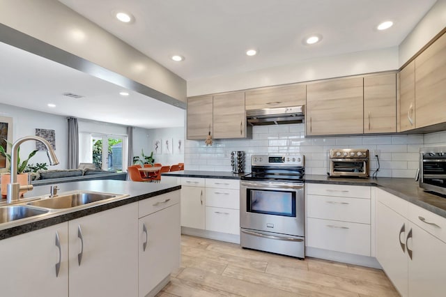 kitchen with under cabinet range hood, a sink, stainless steel electric range, decorative backsplash, and dark countertops