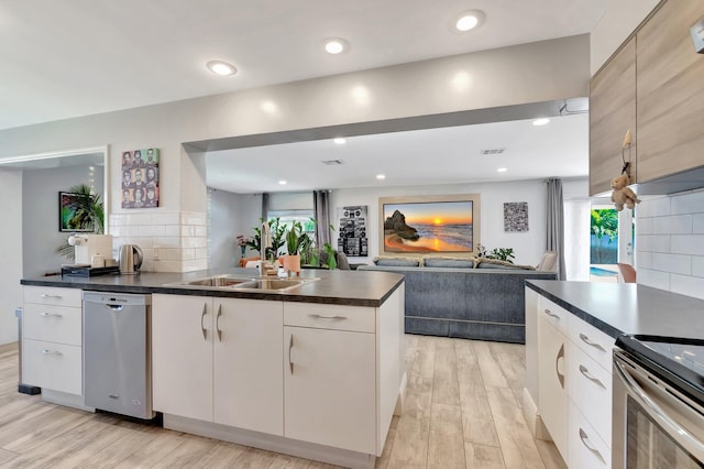 kitchen featuring tasteful backsplash, dark countertops, light wood-style flooring, appliances with stainless steel finishes, and a sink