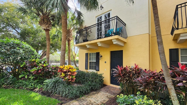 view of exterior entry featuring stucco siding, a balcony, and fence