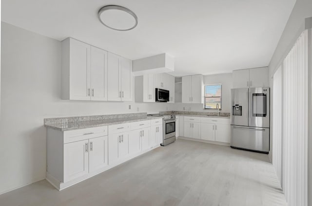 kitchen featuring white cabinets, light wood-style flooring, stainless steel appliances, and a sink