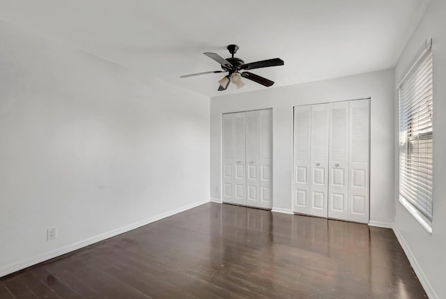 unfurnished bedroom with baseboards, wood finished floors, and multiple closets