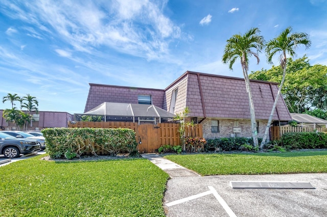 view of front facade with uncovered parking, mansard roof, a front yard, and fence