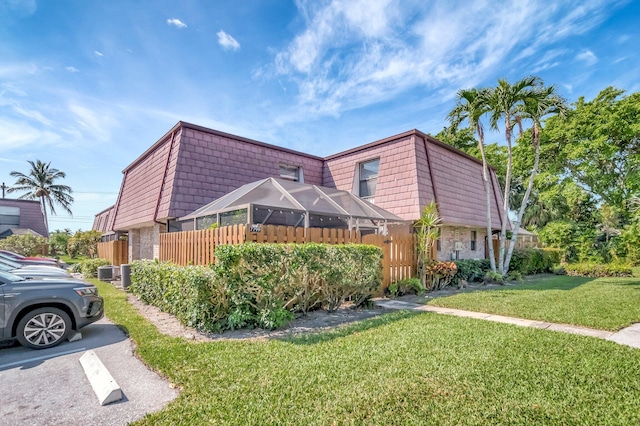 view of side of property featuring uncovered parking, mansard roof, cooling unit, and a yard