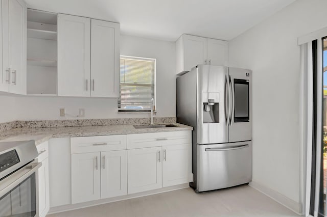 kitchen with open shelves, white cabinetry, a sink, stainless steel fridge, and range