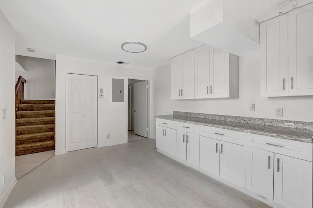 kitchen with light stone counters, light wood-type flooring, electric panel, and white cabinetry