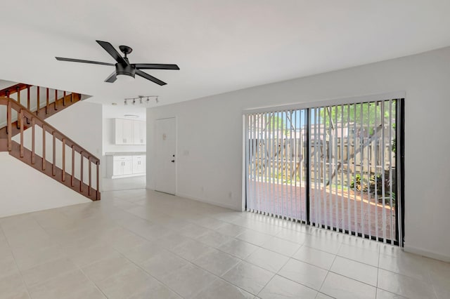 unfurnished living room with light tile patterned floors, a ceiling fan, baseboards, stairway, and track lighting