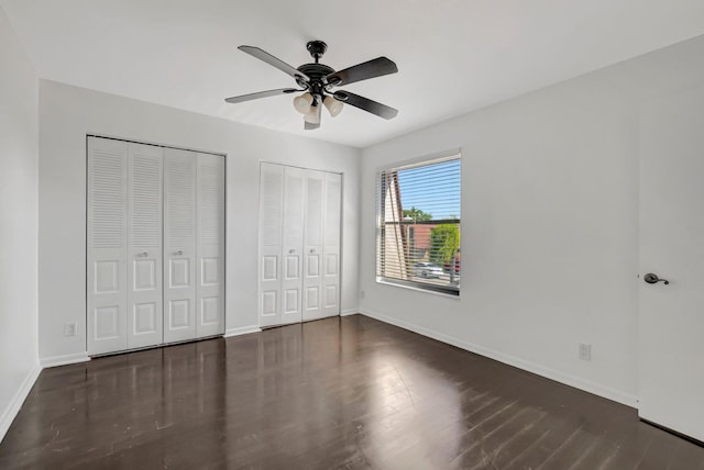 unfurnished bedroom featuring wood finished floors, two closets, a ceiling fan, and baseboards